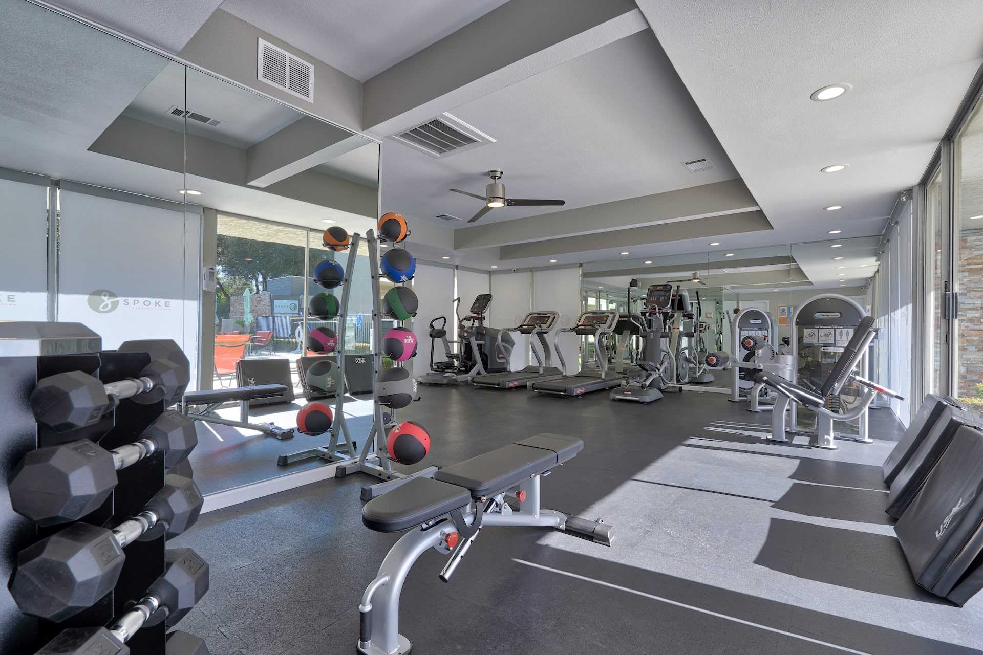large fitness room with floor to ceiling windows, free weights, medicine balls, treadmills, and elliptical machines.