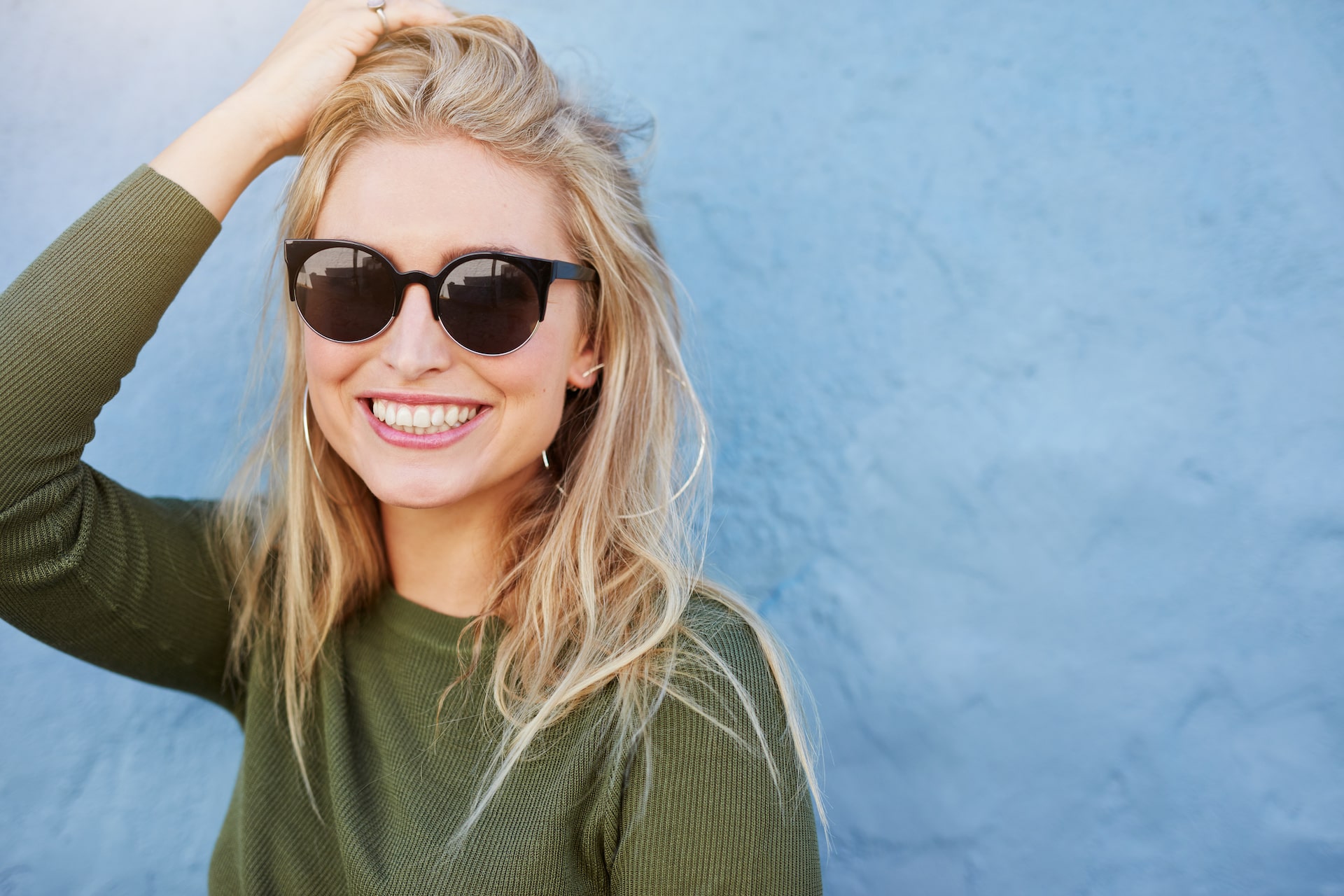 Woman in sunglasses smiling in front of blue wall