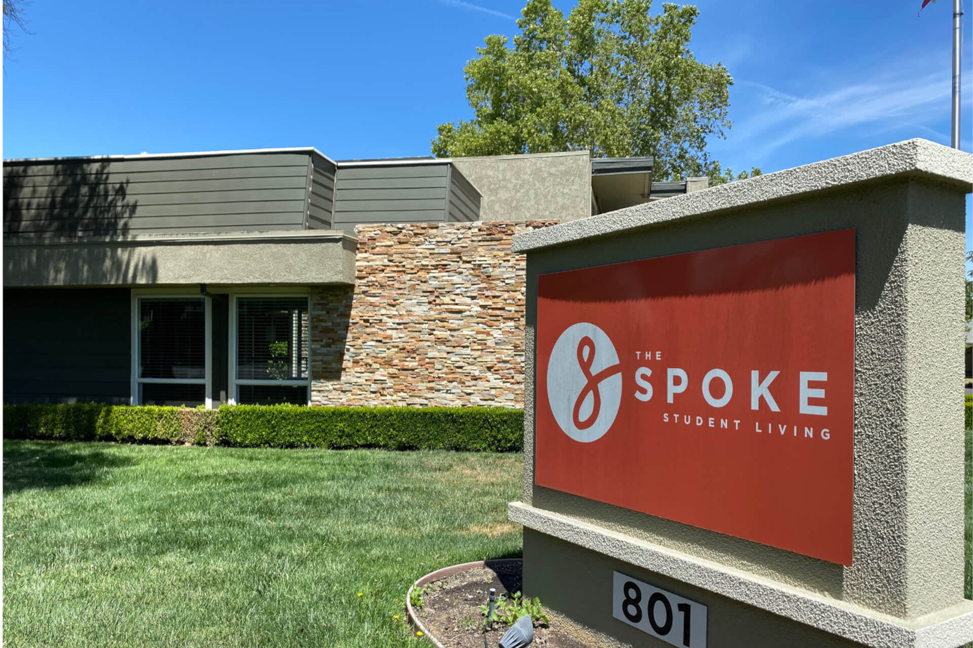 stucco sign for The Spoke Student Living with leasing office in background.